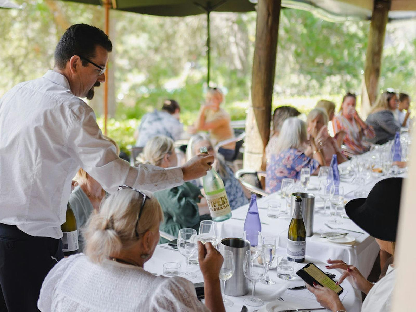 Adrian serving local wine at an outdoor fine dining table filled with delicious food with guests.