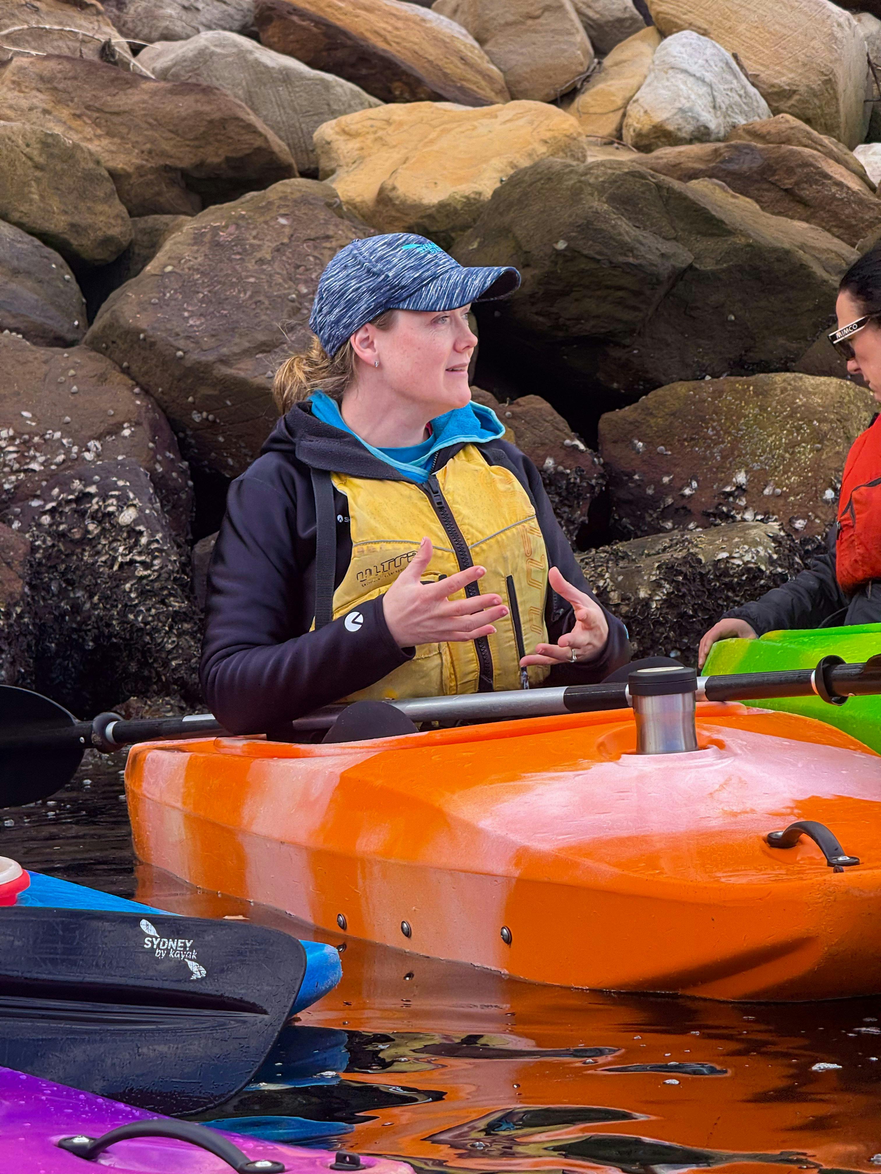 Laura Stone sitting in orange kayak sharing Sydney's best stories including the Harbour Bridge.