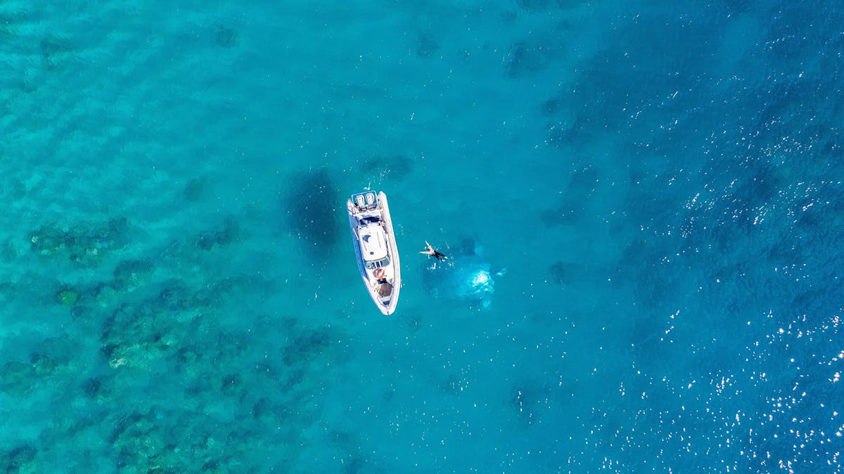 Aerial photo of a boat and swimmer on the surface of the water with a turtle sculpture visible below