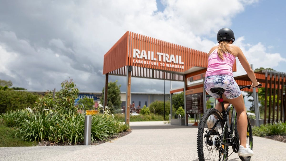 A woman cycling at the entry to the Caboolture to Wamuran Rail Trail