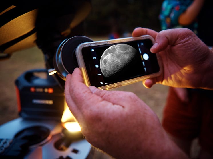 Hands taking a photo of the moon through the telescope
