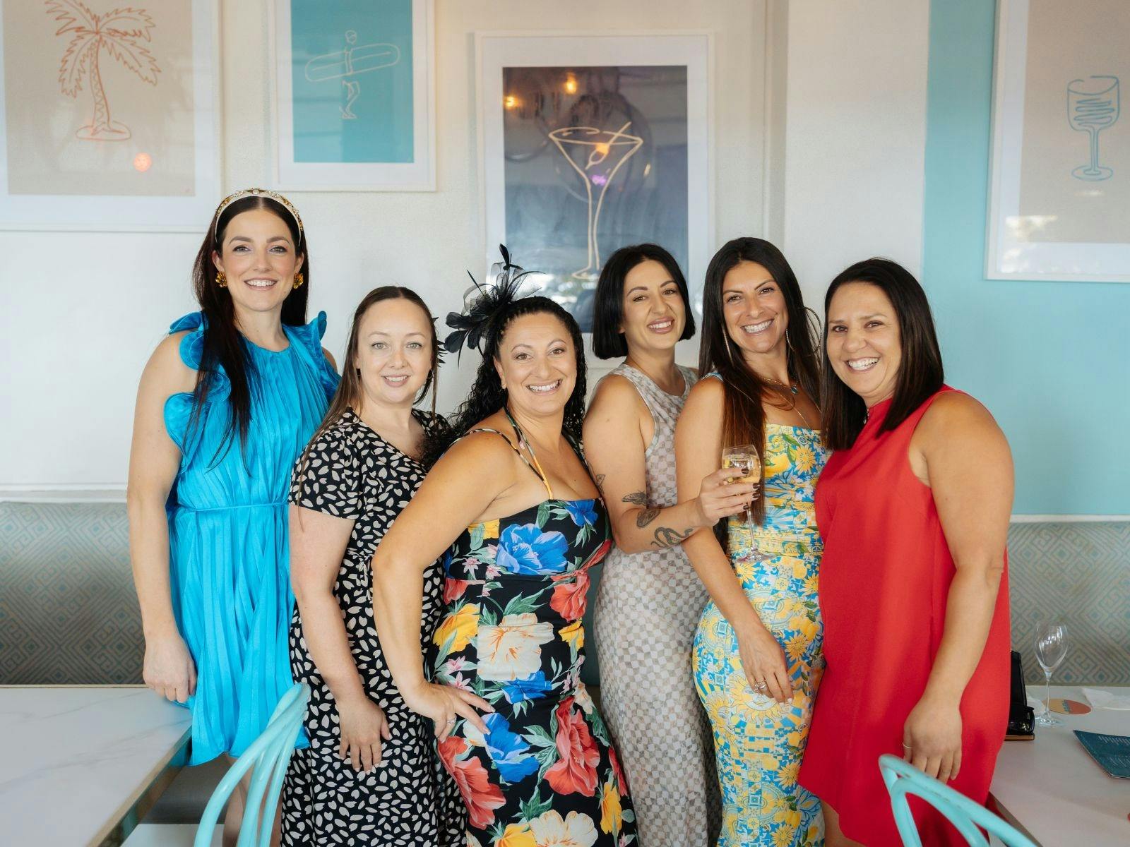 Group of six women dressed for Melbourne Cup smiling together inside Pepe’s on the Beach.