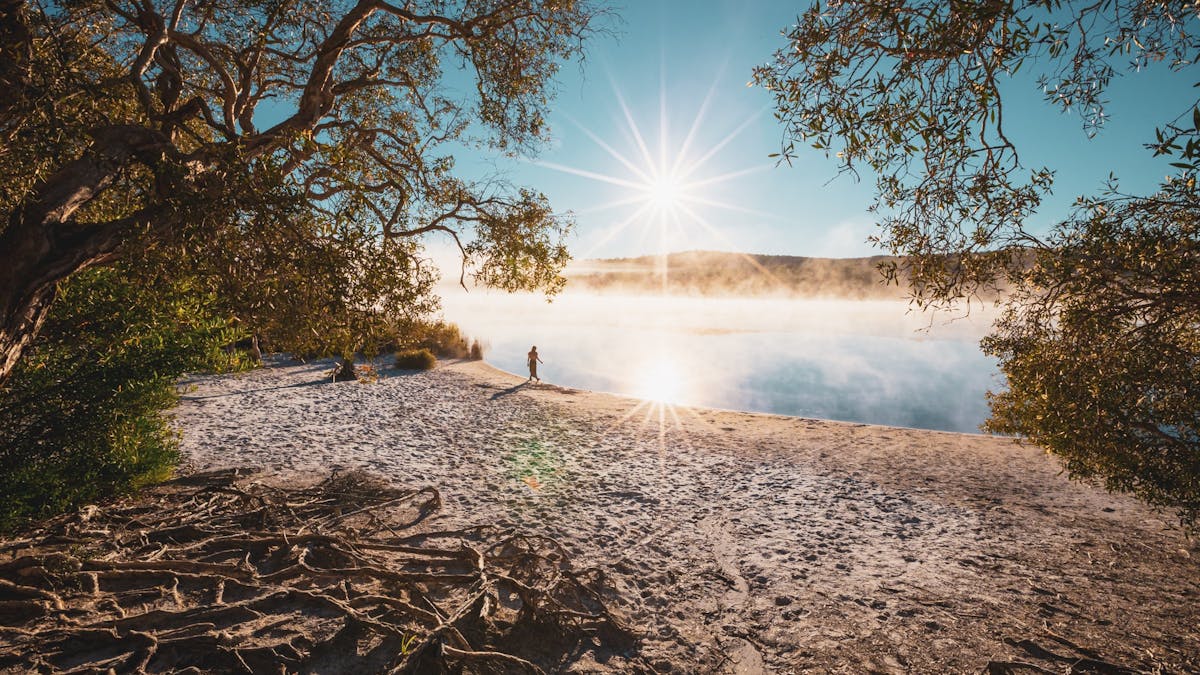Woman walking by misty Brown Lake with morning sunshine on Minjerribah
