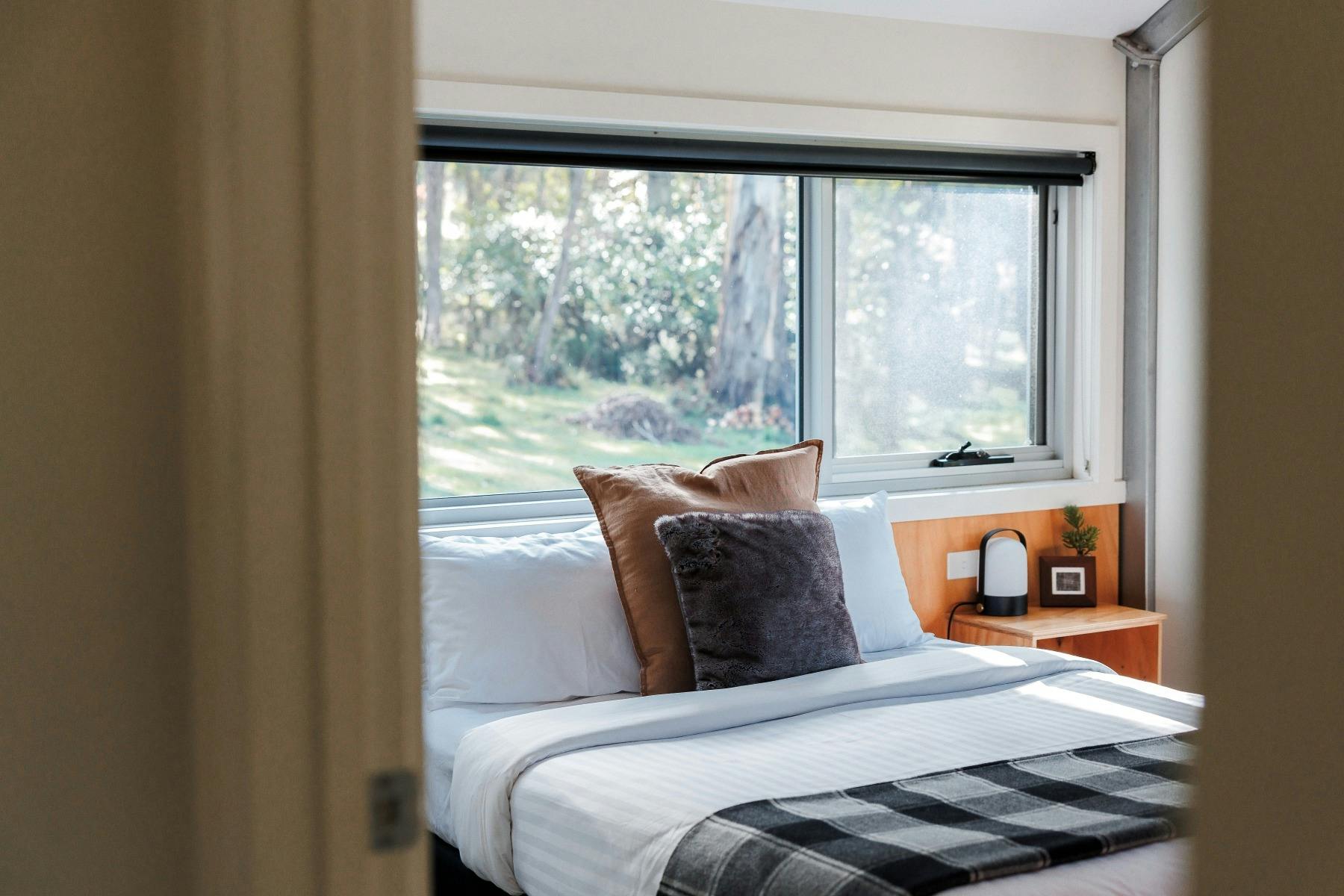 Warm toned bedroom with a queen bed, window over bed with views of bushland.