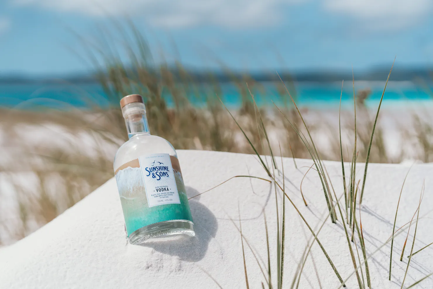 A bottle of our Original Vodka lying in white sand on the beach