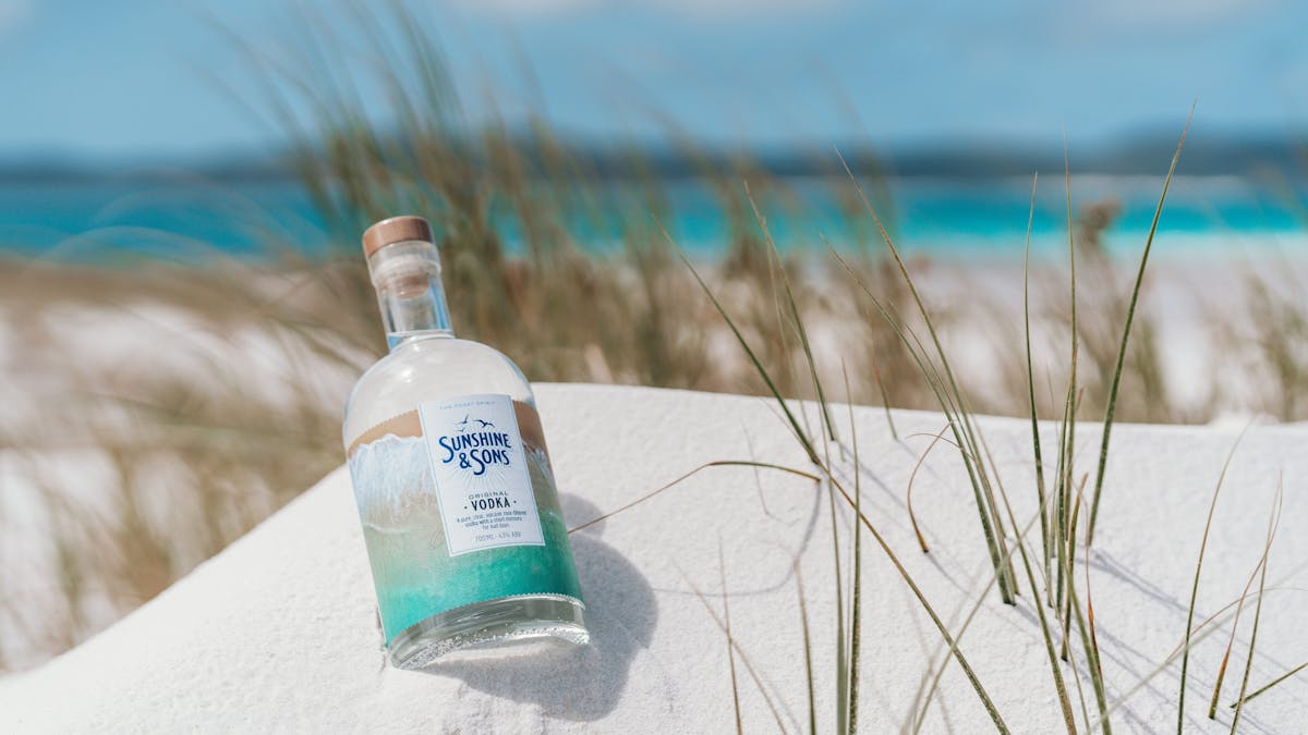 A bottle of our Original Vodka lying in white sand on the beach