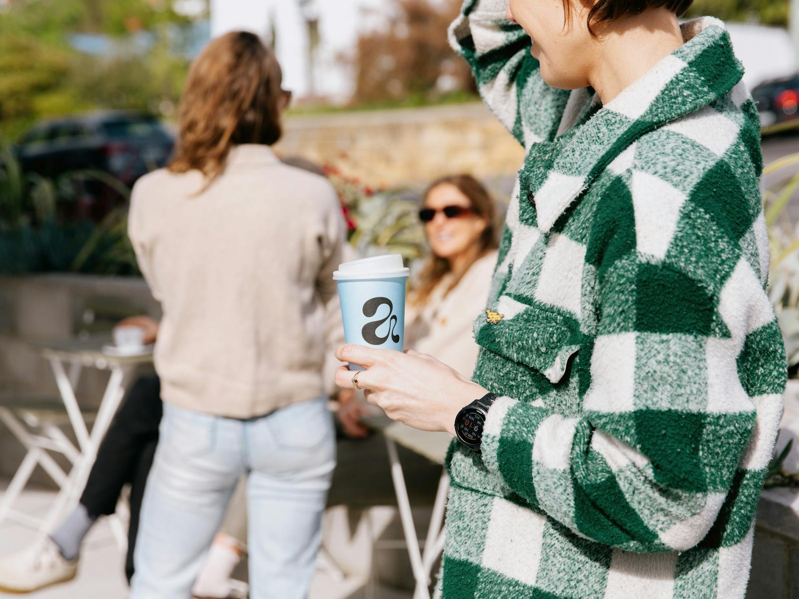 Woman holds an Abercrombie Coffee takeaway cup, standing outside in the sunshine.