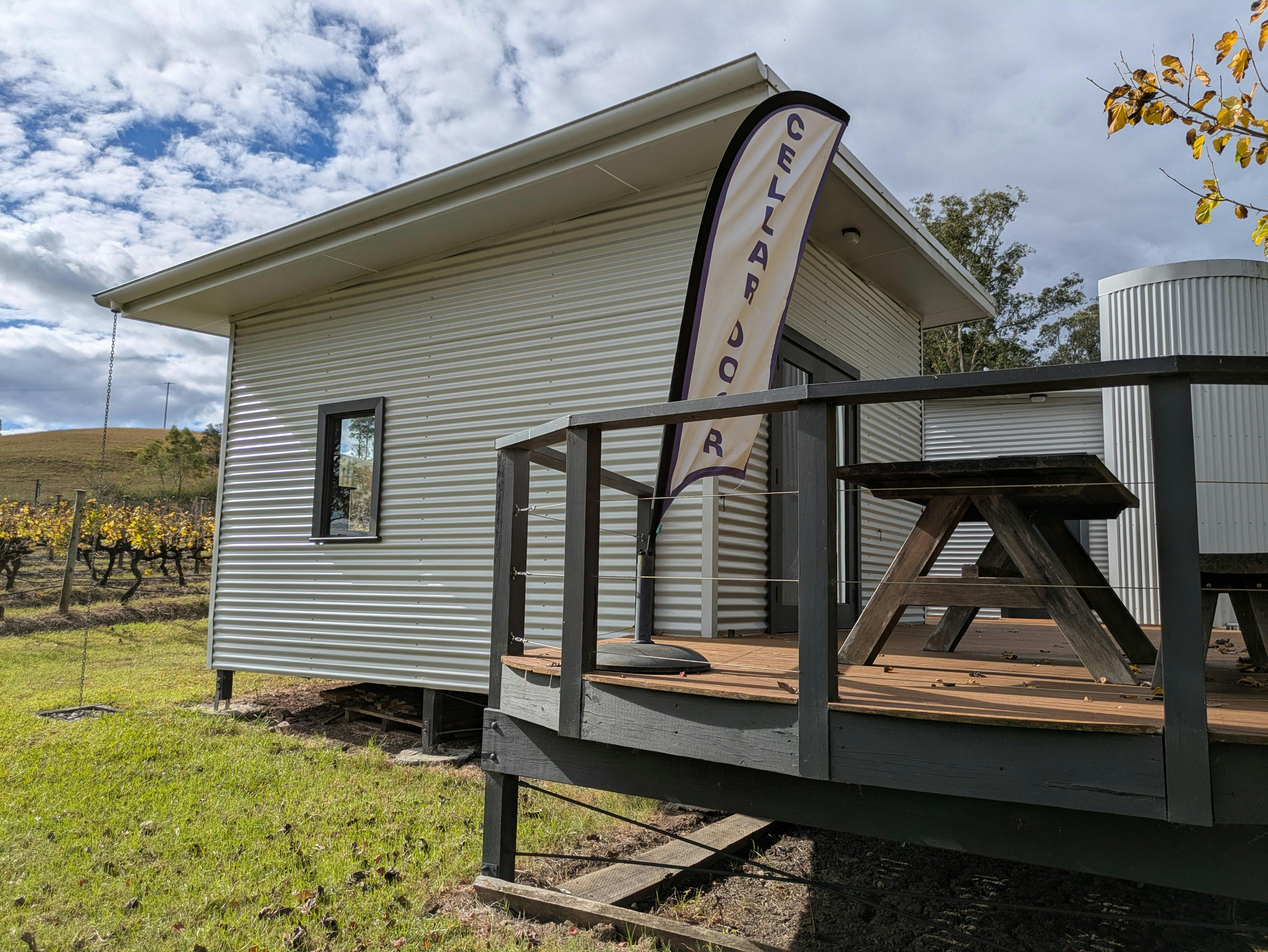 Cellar Door outside Decking area with wooden table & bench seat. Vines are visible in the background