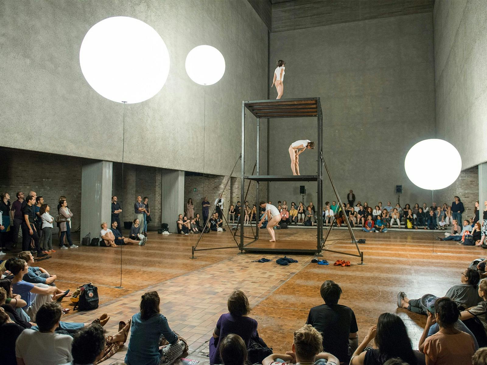 Three dancers are standing on a structure, similar to scaffolding, it has 3 levels