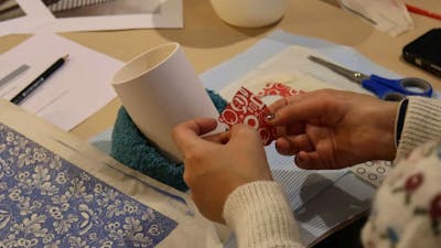 A close up shot of a pair of hands applying a red decal to a white ceramic cup