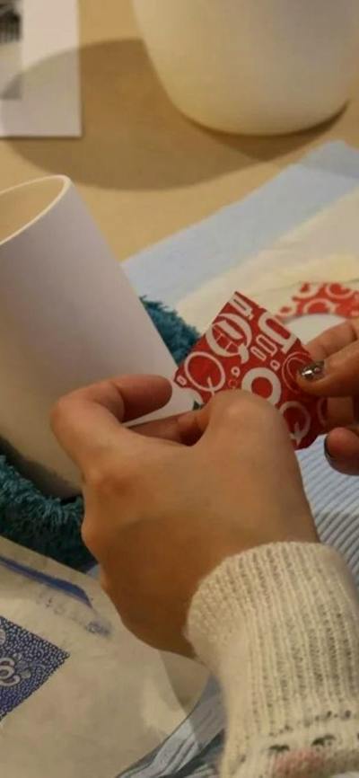 A close up shot of a pair of hands applying a red decal to a white ceramic cup