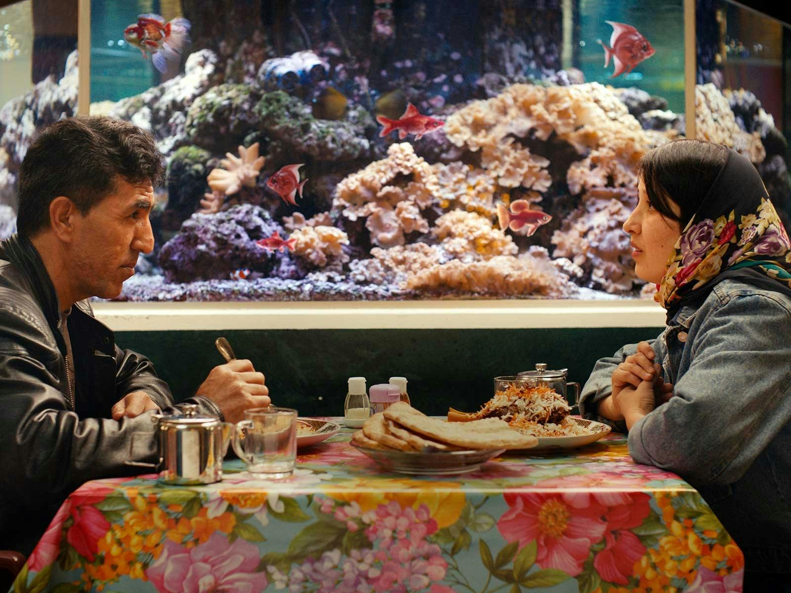A couple site opposite at a colourful table next to a colourful fish tank
