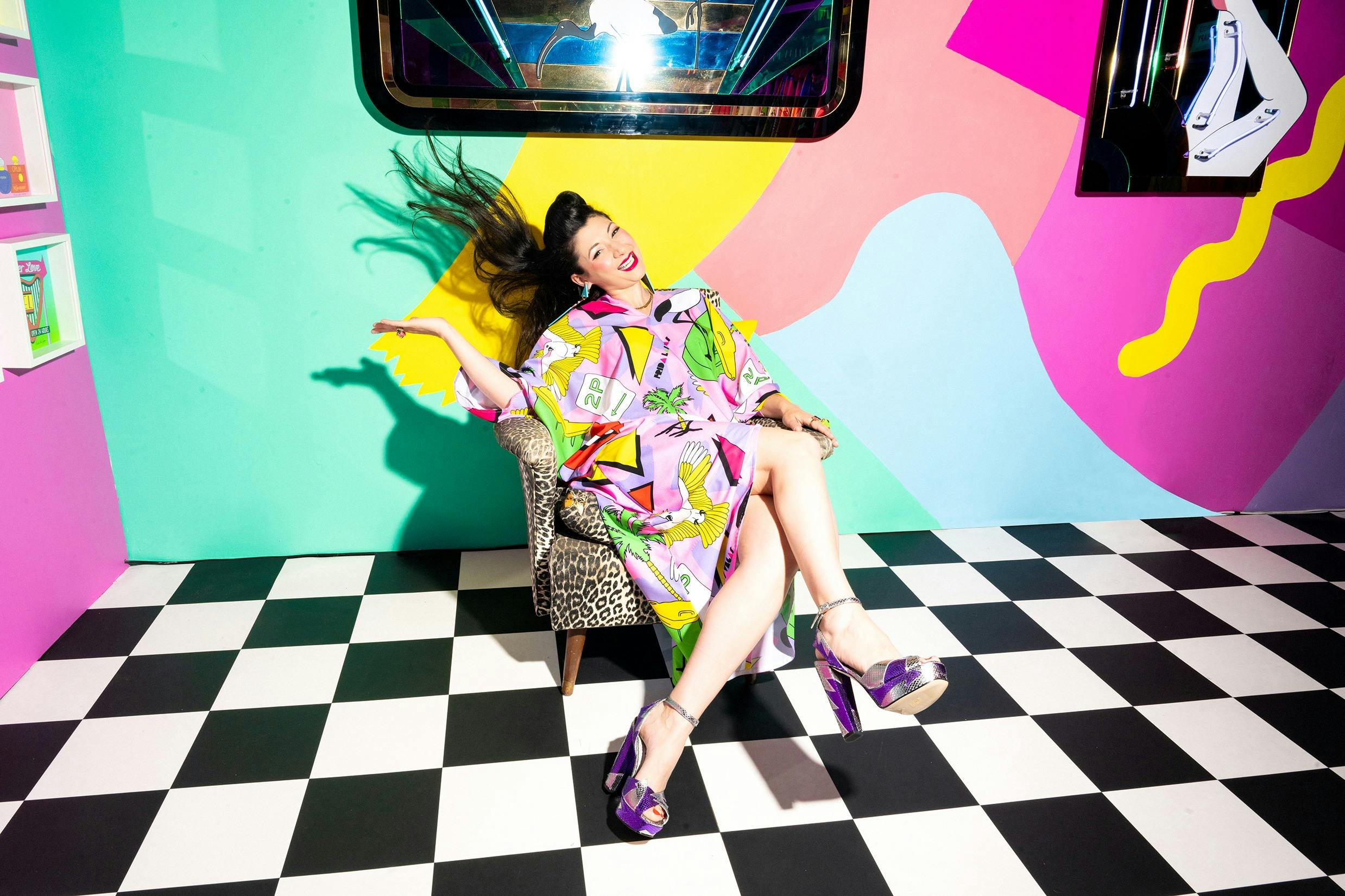 Frida Las Vegas sitting in a chair and wearing a brightly coloured glamour sack, swishing her hair a