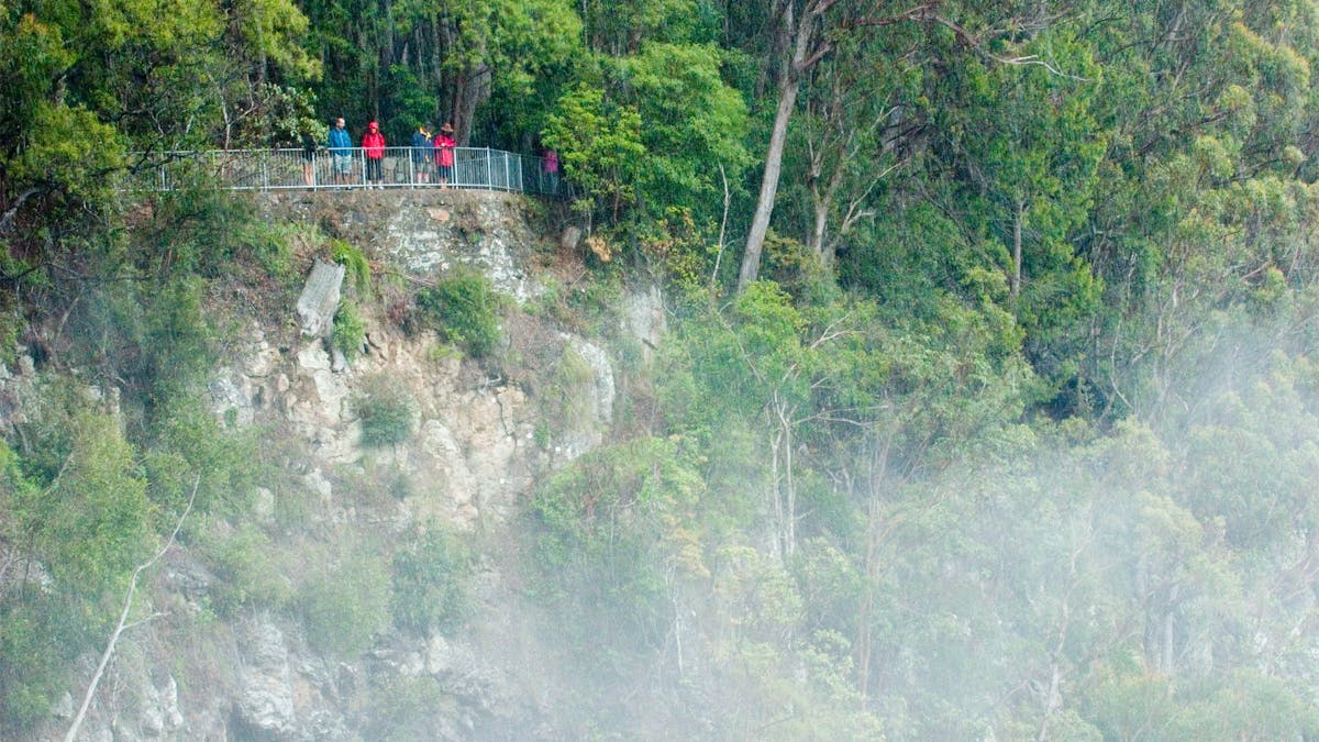 People standing on lookout on cliff face shrouded in mist from the falls.