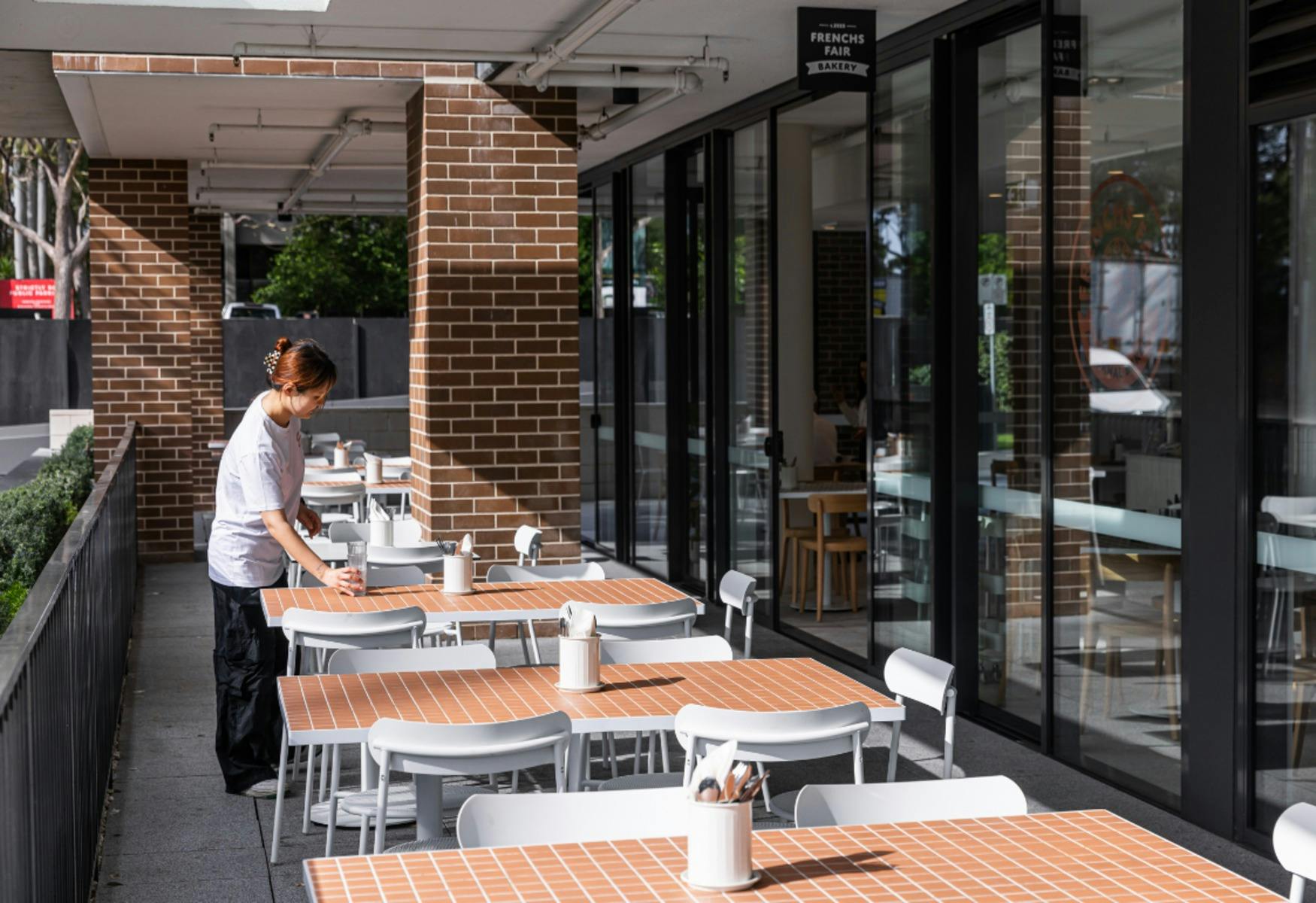 덮인 파티오 구역에 카페 테이블이 놓여 있고 웨이트리스도 보입니다.