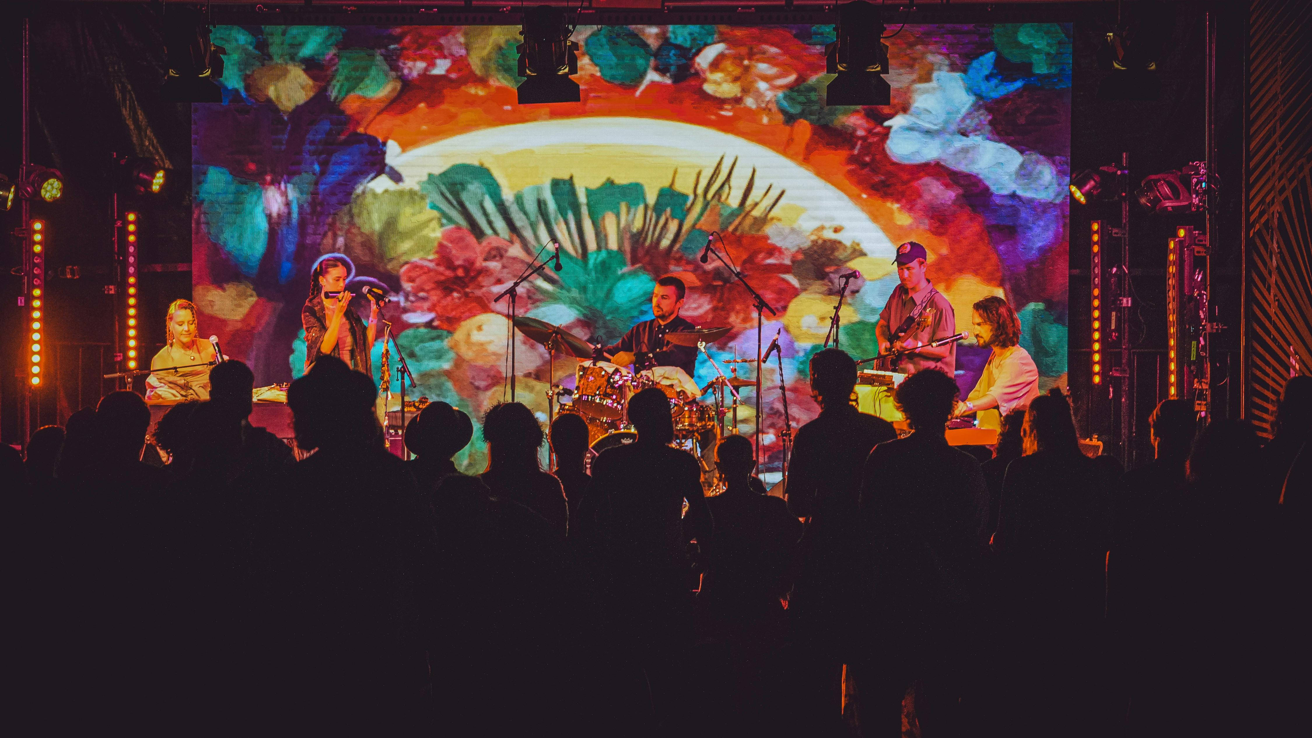 A crowd of people shot from behind enjoying a show from a brightly lit stage from the 2025 festival.