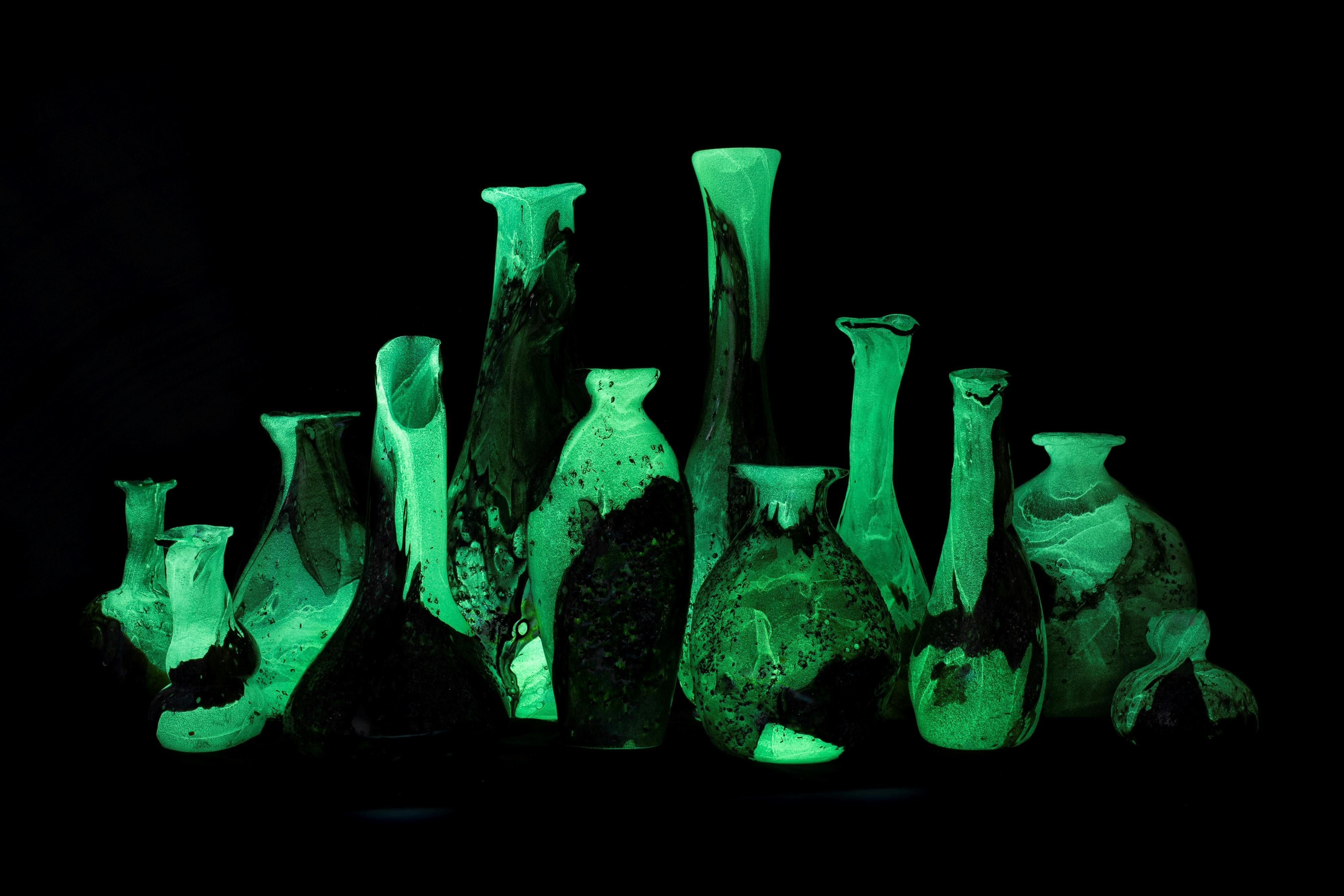 A collection of glass artworks glow green against a black background