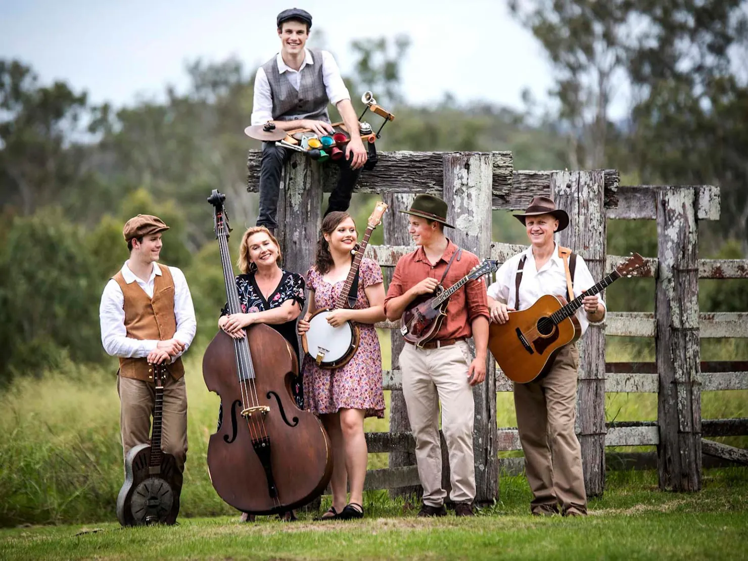 A group of musicians holding different music instruments standing on a farm.