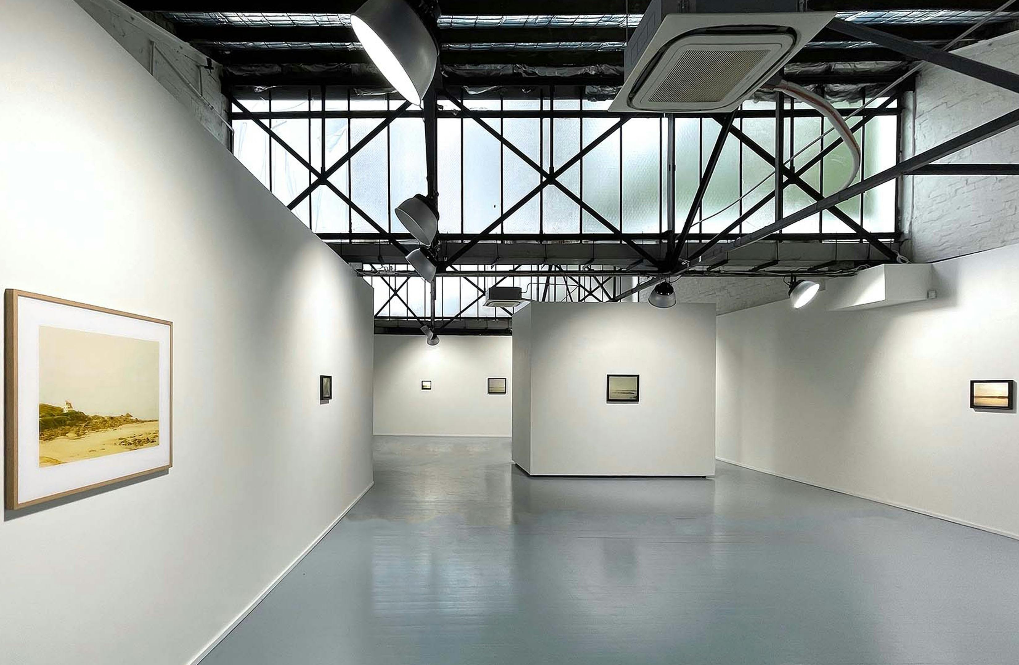 Interior shot of a gallery space, with naturally lit white walls and a high ceiling.