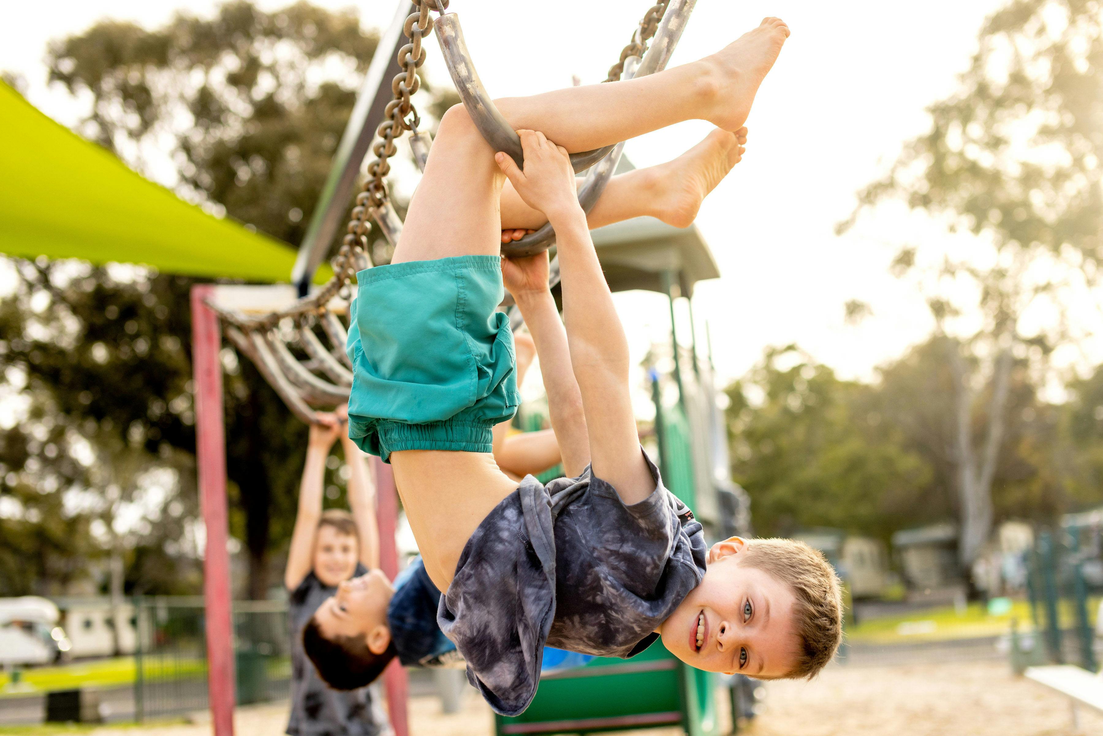 Two boys hanging on the monkey bars in the playground.