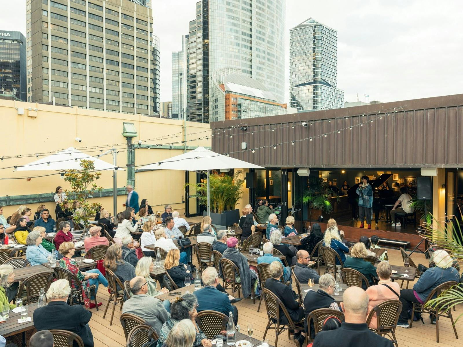 Image of the Library Bar - rooftop bar with people seated watching a performer on stage