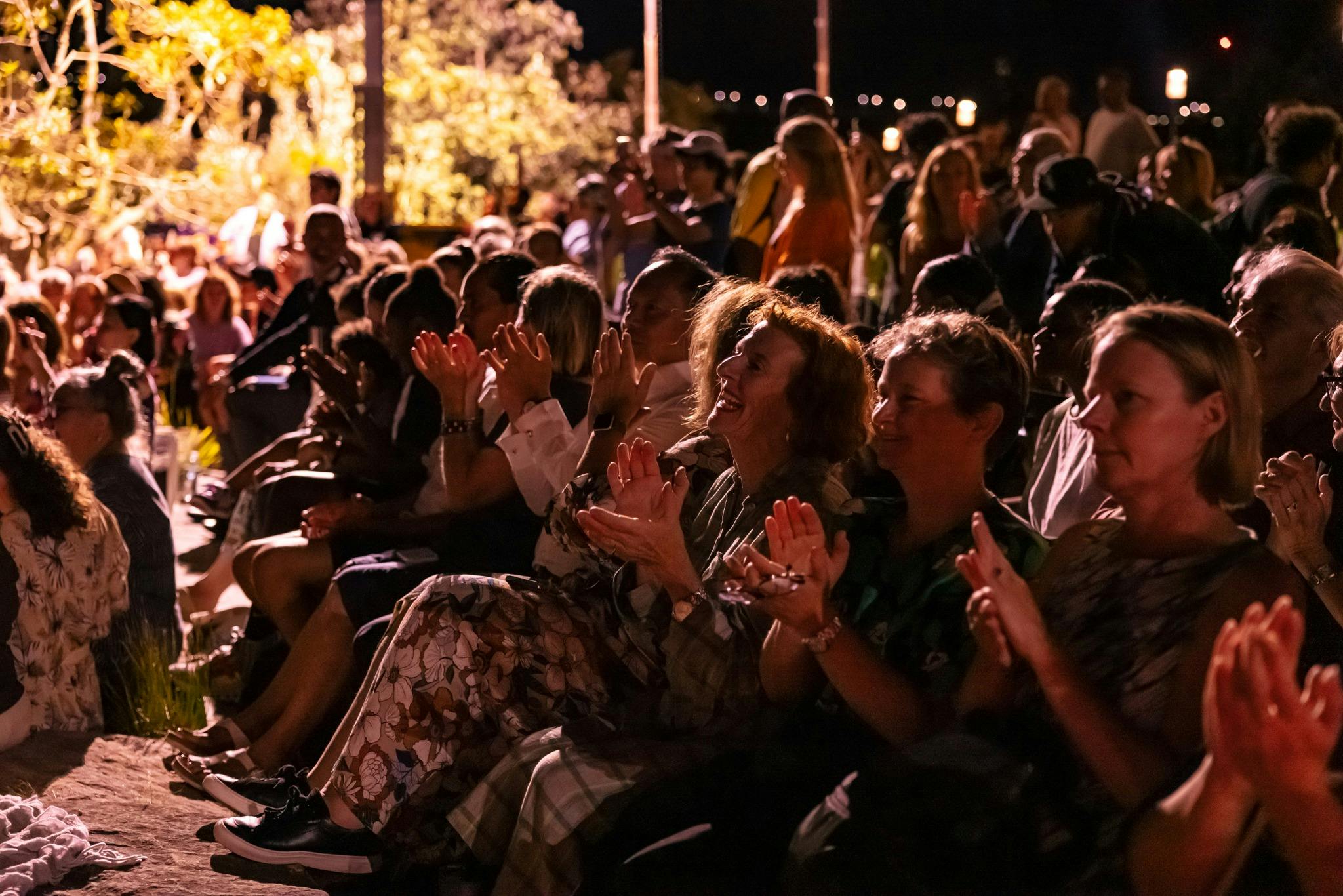 Seated audience applauding outdoors at night