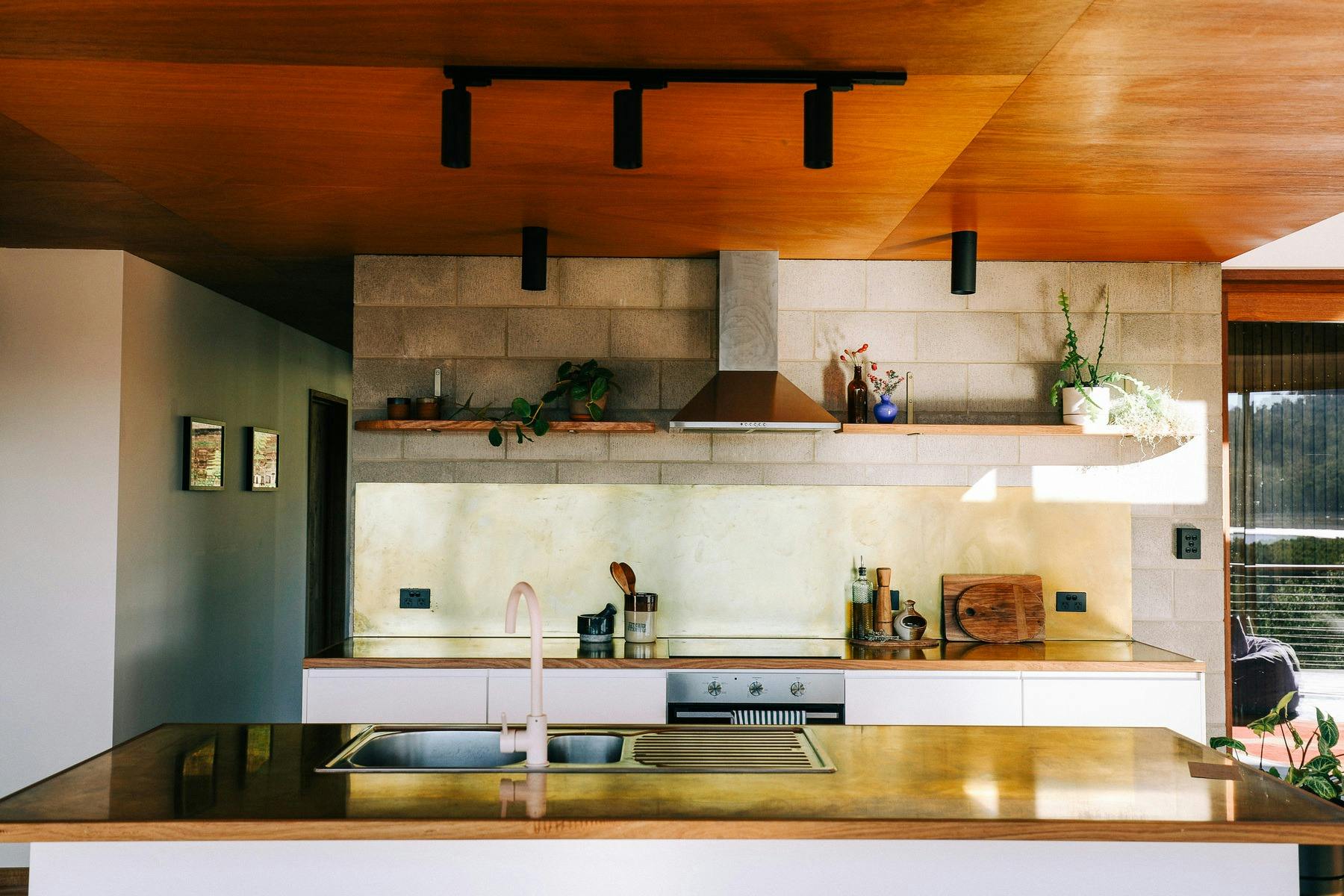 A modern kitchen with brass bench tops and pink tap, and besser-block brick walls.