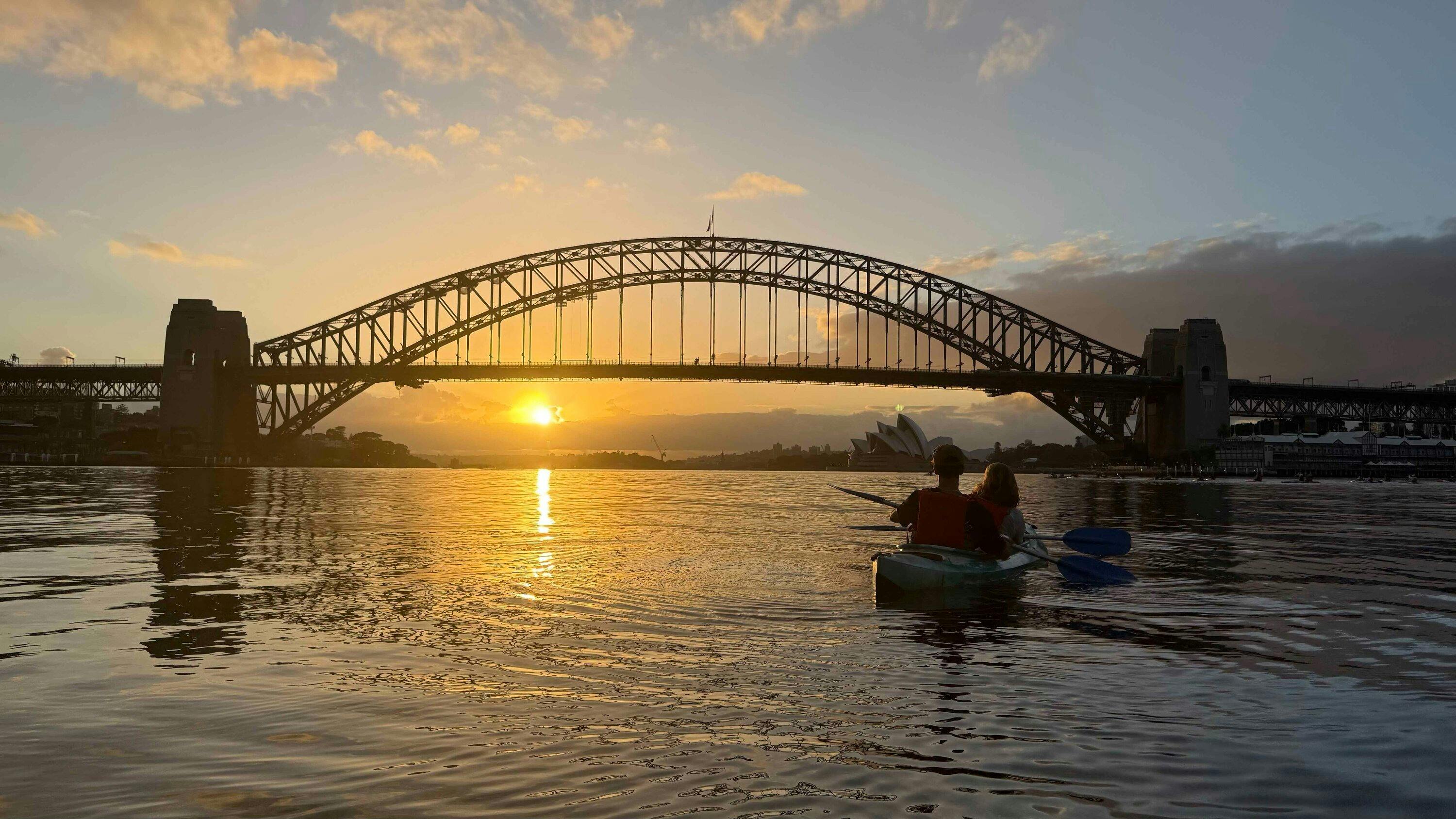 日出時分，皮划艇運動員的身影在雪梨海港大橋的拱門下勾勒出來。