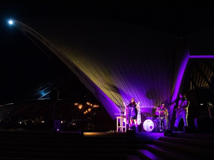 A band of 3 people singing in front of the Sydney Opera House sails