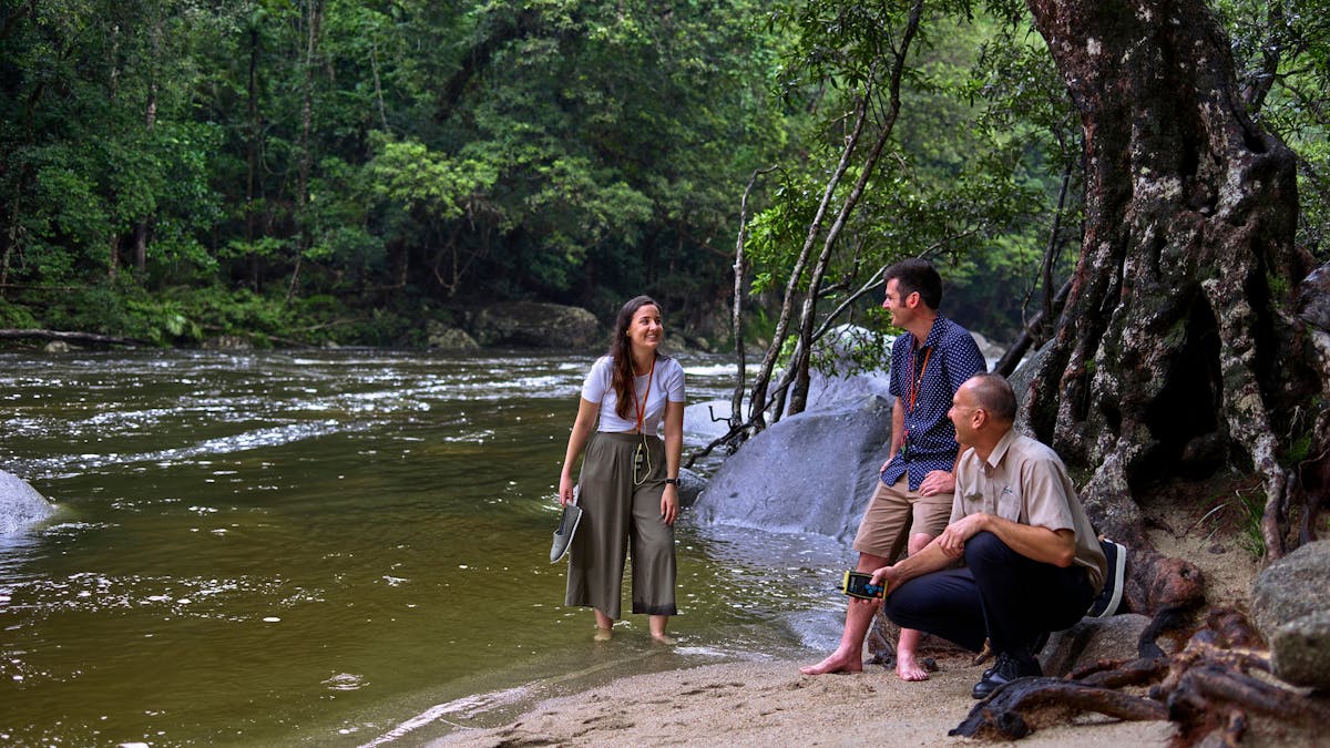 Driver Guide with interacting with passengers on shore of Mossman Gorge River.