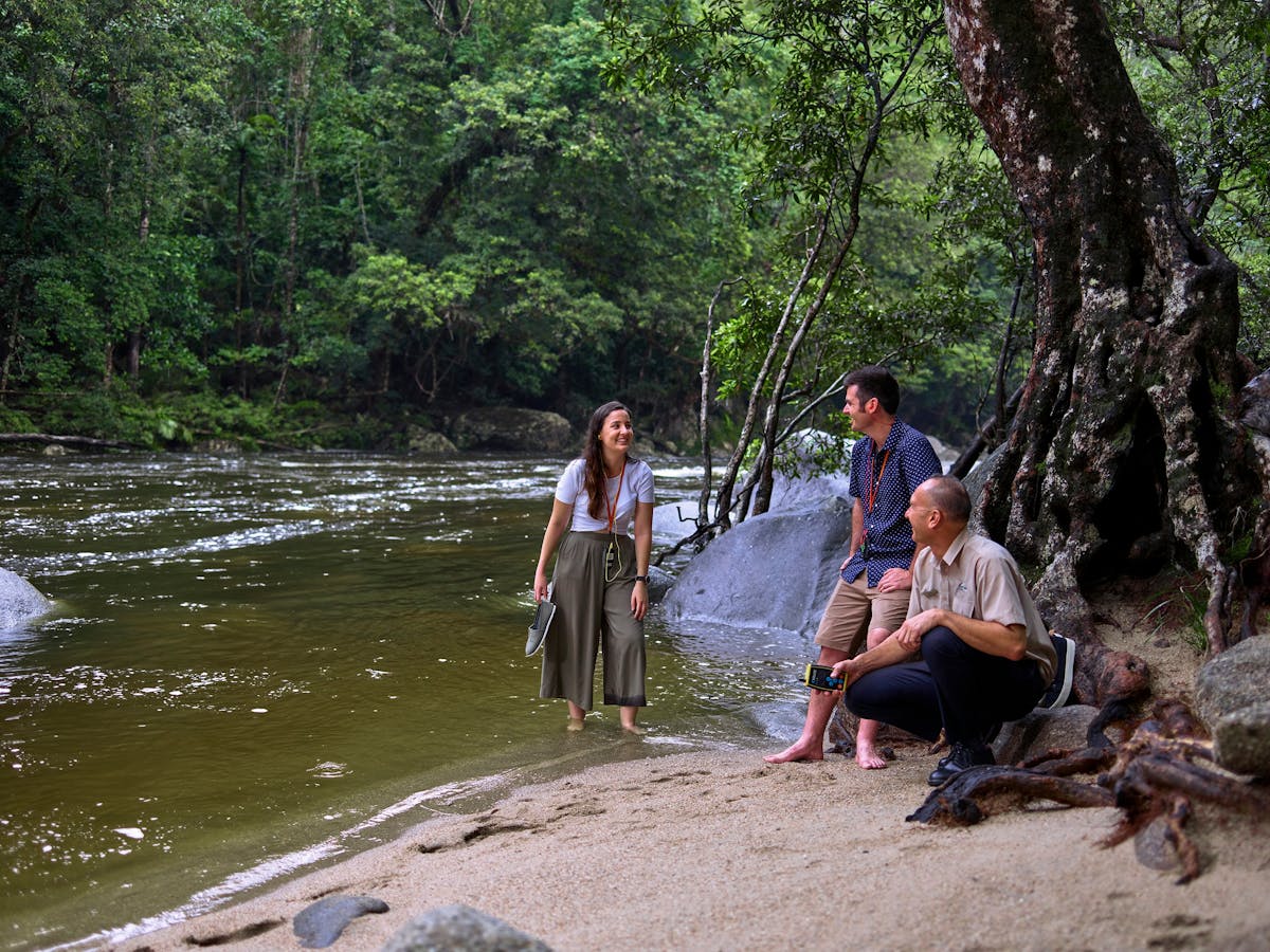 Driver Guide with interacting with passengers on shore of Mossman Gorge River.