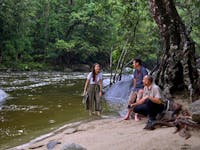 Driver Guide with interacting with passengers on shore of Mossman Gorge River.