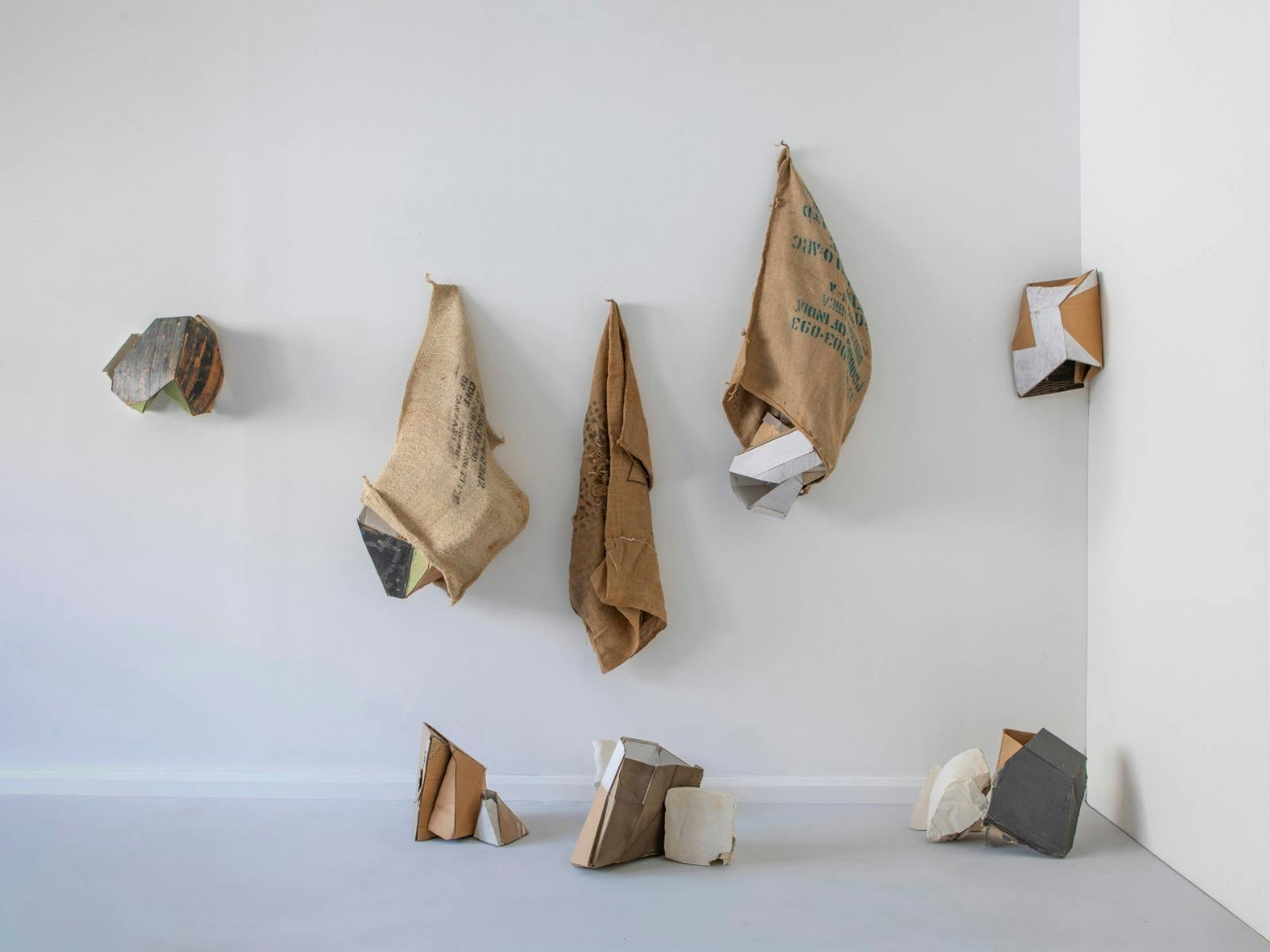 Series of hessian sacks, packaging cardboards, plaster and other materials on a wall.