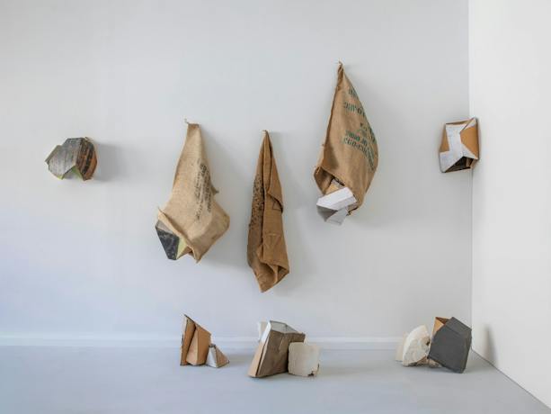 Series of hessian sacks, packaging cardboards, plaster and other materials on a wall.