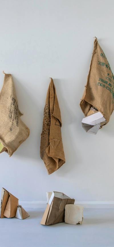 Series of hessian sacks, packaging cardboards, plaster and other materials on a wall.