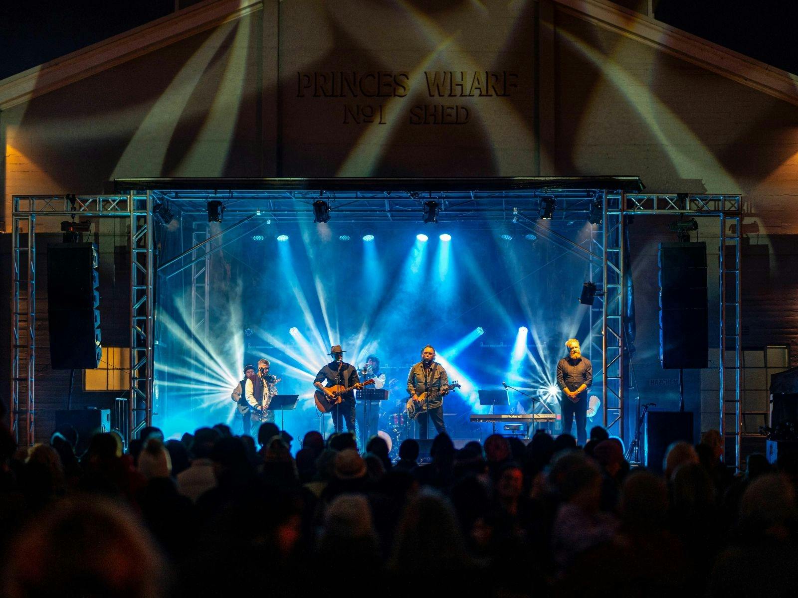 A colour photograph with lots of white and cool blue lighting that highlights 4 performers playing