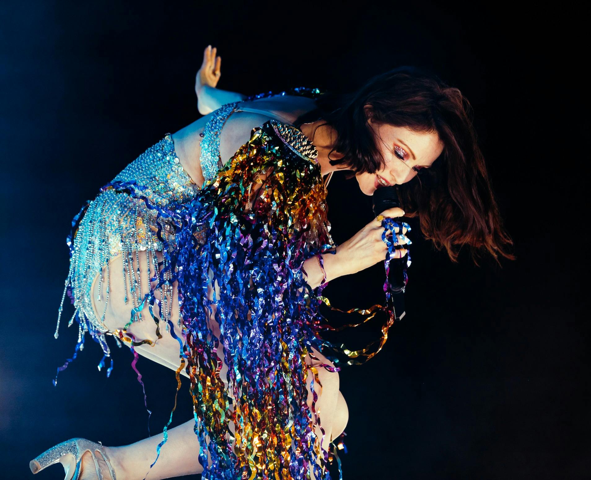 woman on stage signing into microphone with sparkly clothing