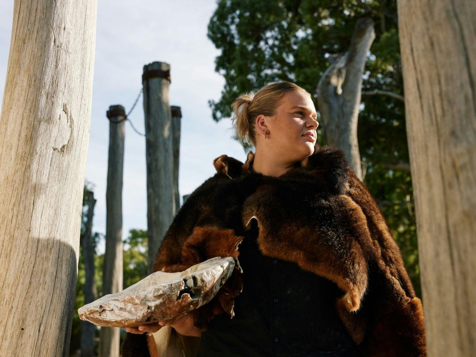 A woman wearing a possum skin cloak and holding an ochre bowl