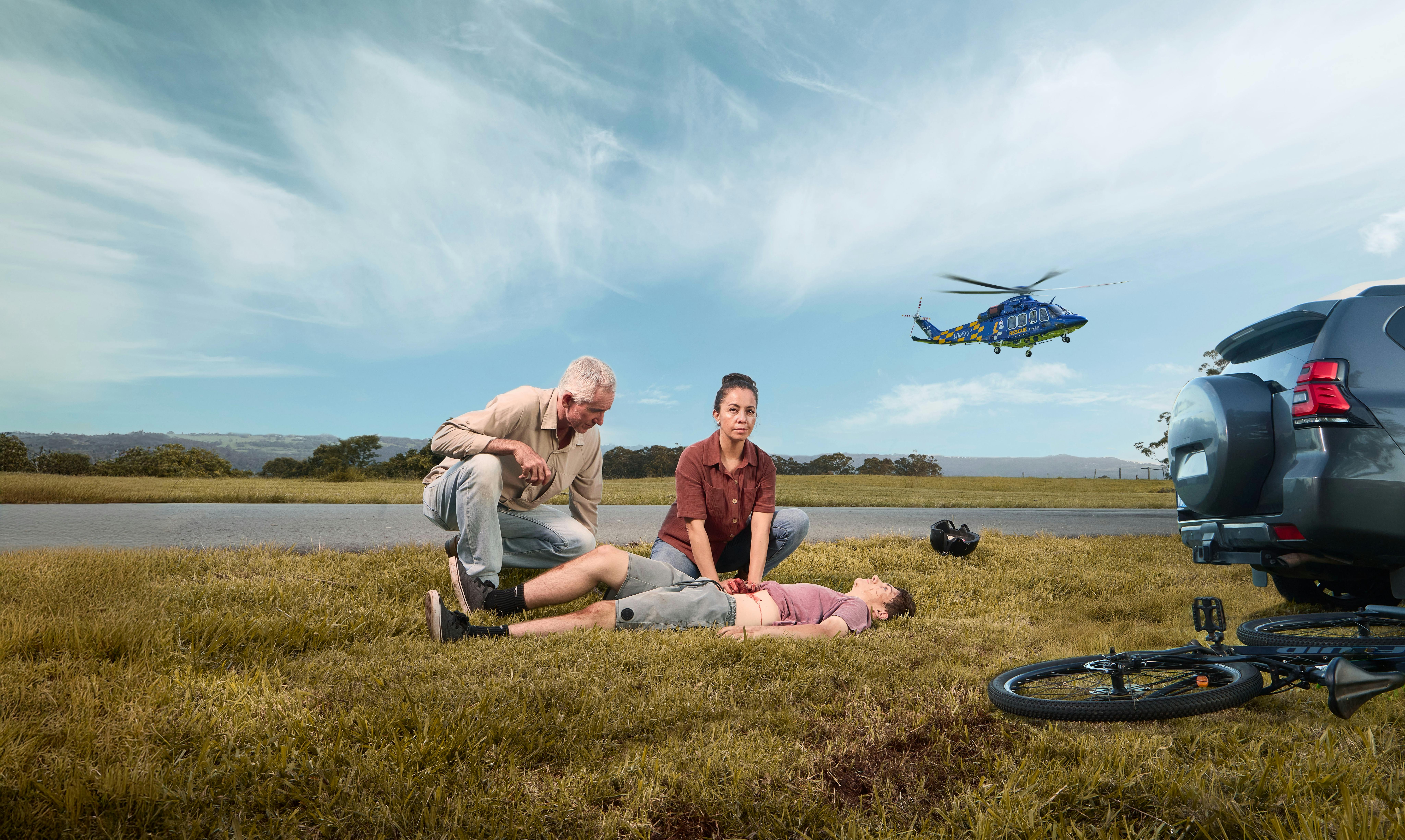 Man and woman helping child in accident on side of road with helicopter in background