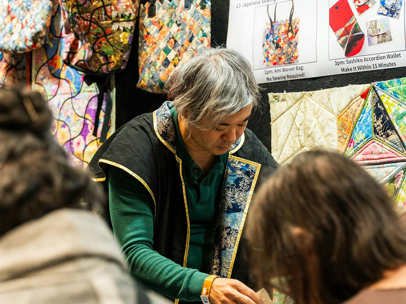 Quilt vendor Exhibitor chats with visitors in front of colourful quilt displays.