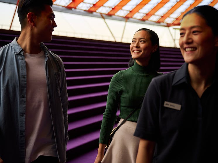 Tour guide leading man and woman down the purple steps in the Concert Hall Northern Foyer