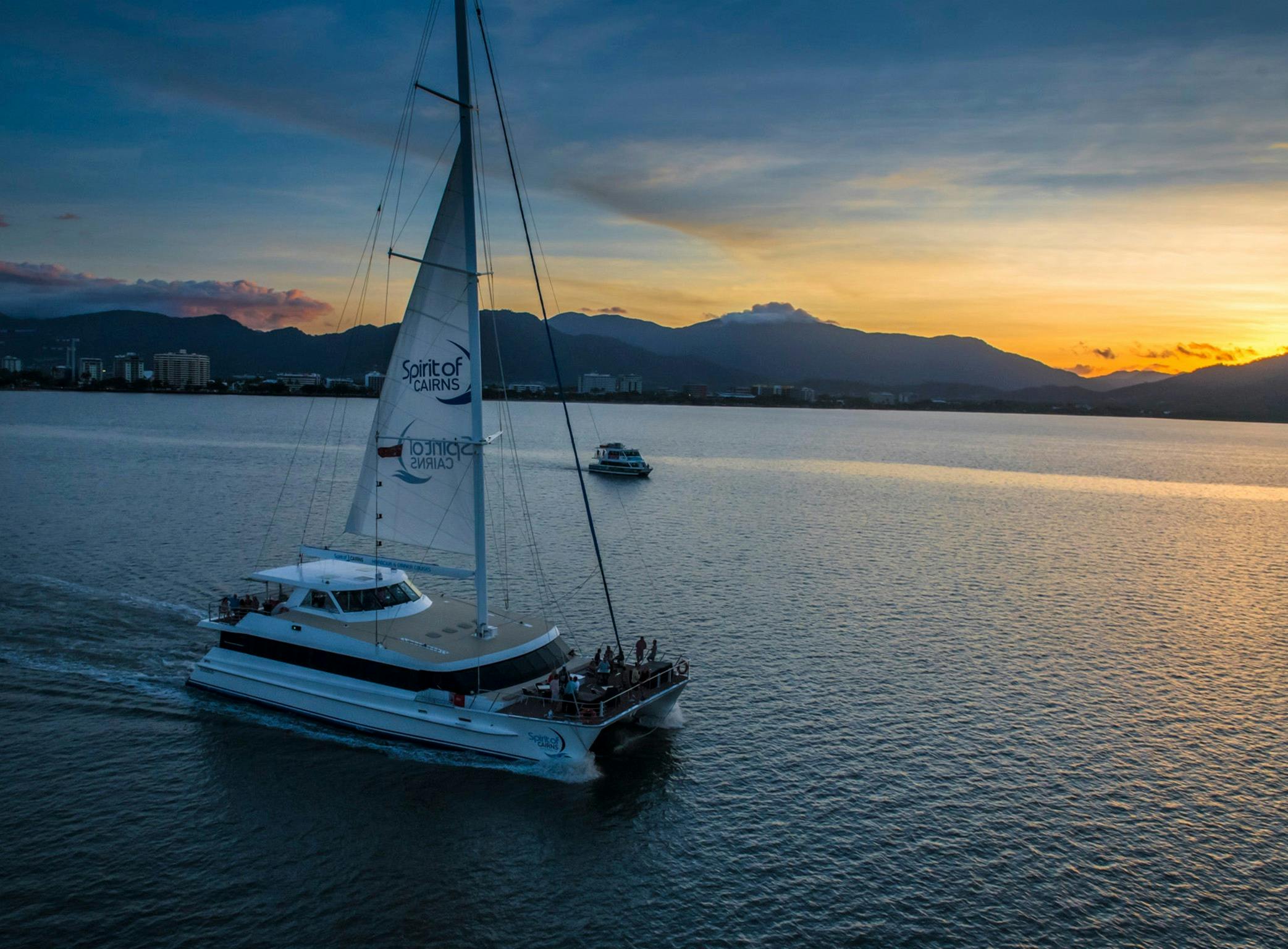 Catamaran sailing down river with mountains and sunset in background