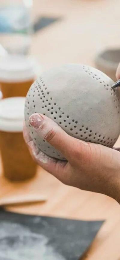Hands hold a clay sphere, poking holes in with a tool for decoration