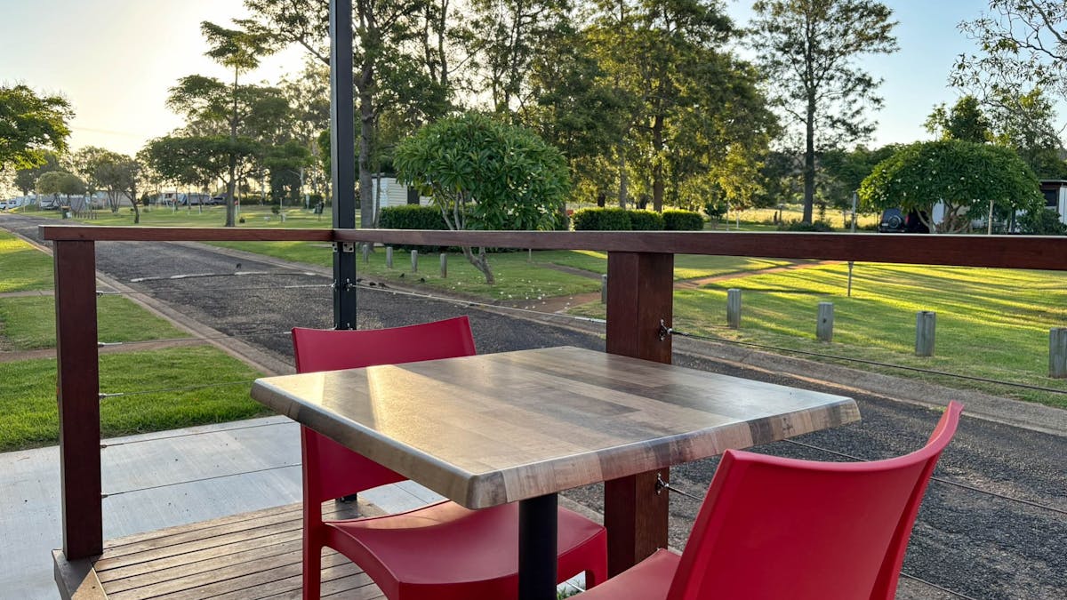 Cabin deck with outdoor table and chairs overlooking green lawns and trees at Yarraman Caravan Park