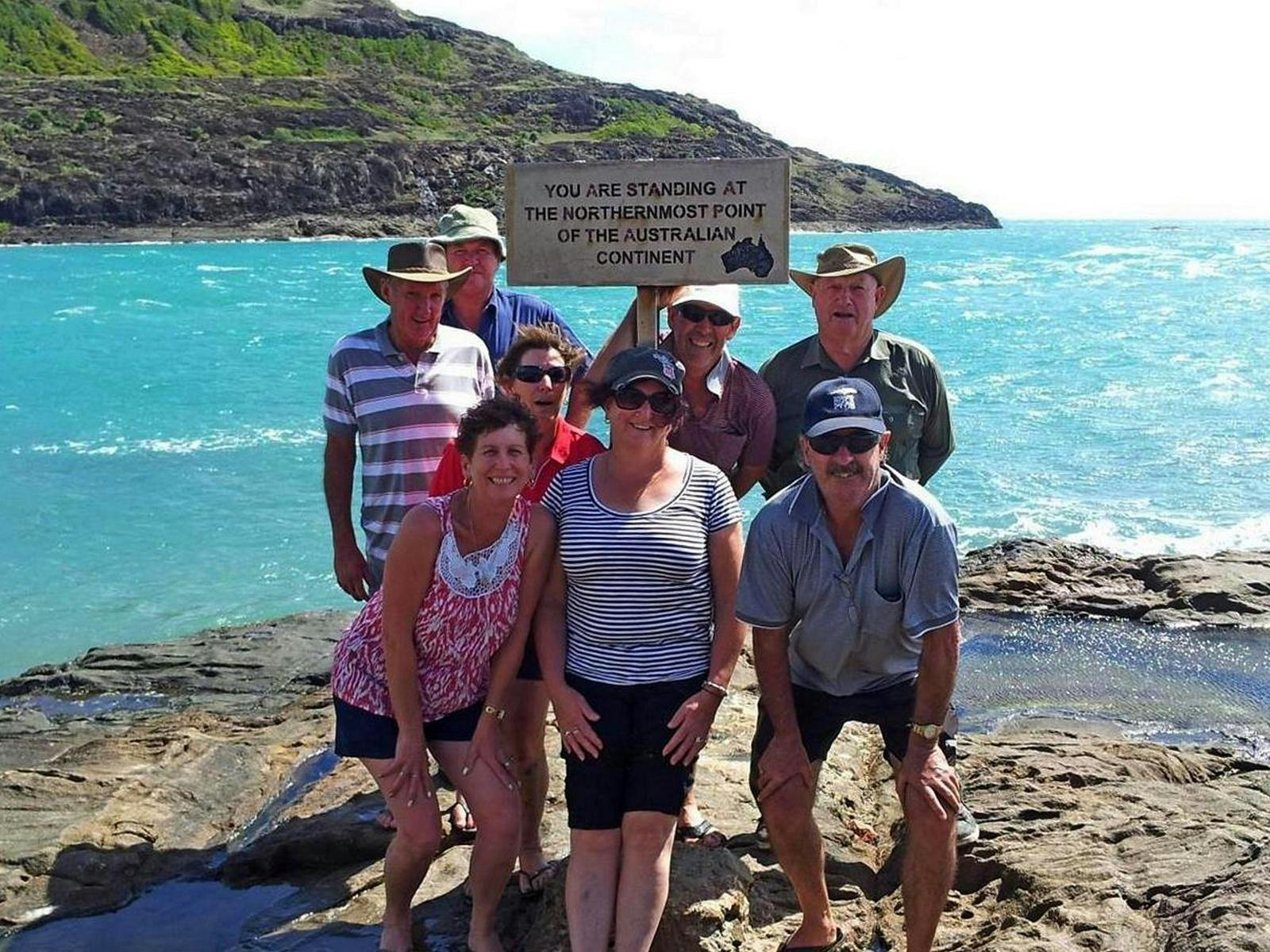 Tour group posing for photos by the sign at the tip of Cape York with York Island in the background.