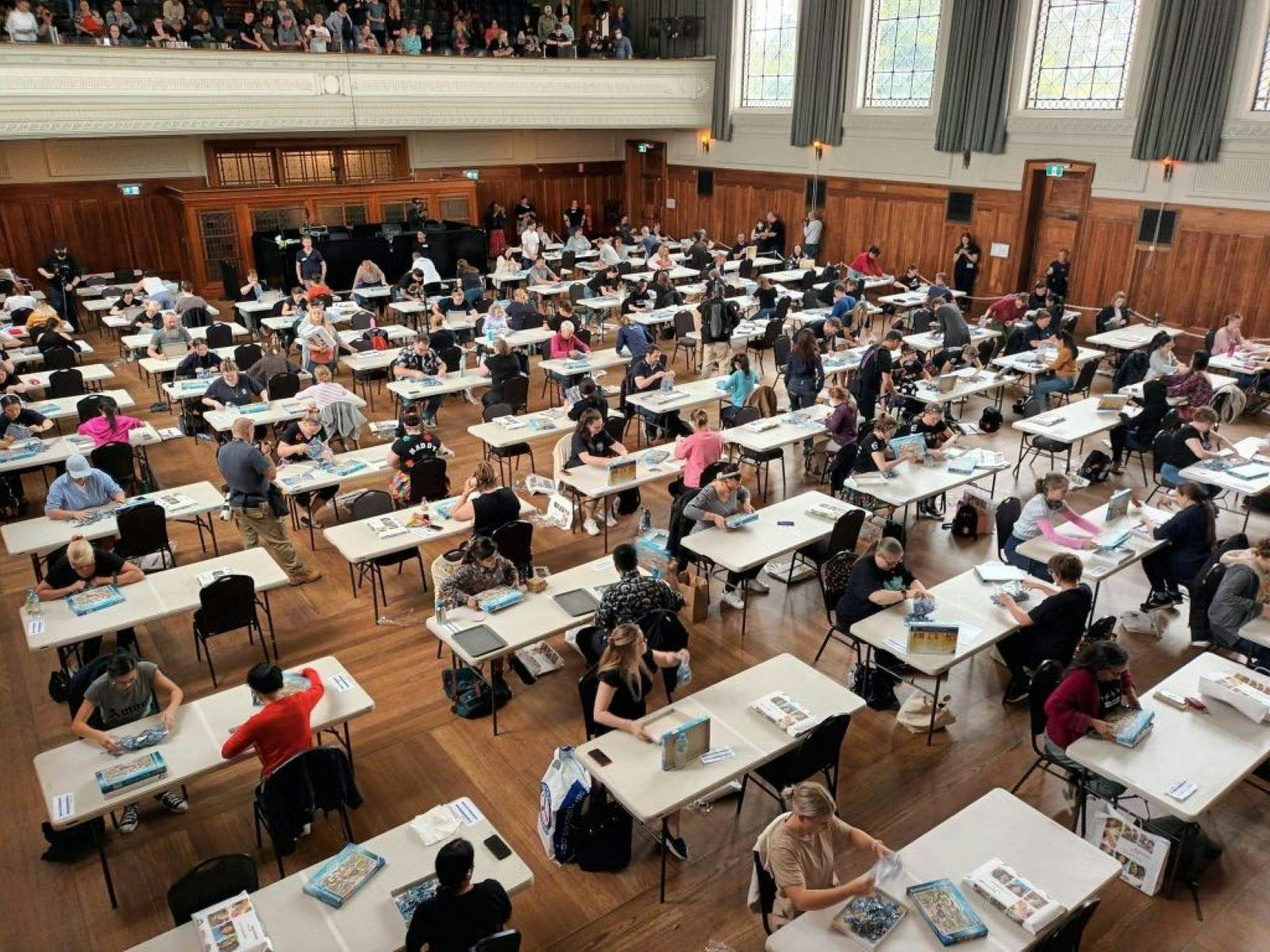 A large room with lots of people sitting at tables completing puzzles A large room with lots of people sitting at tables completing puzzles