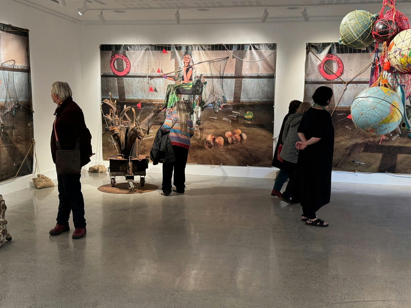 People in the gallery looking at large photos on the walls, sculptures from tree roots and globes