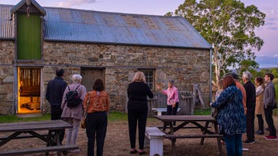 People gather out the front of a stone stable. The light spills out from the doorway as the sun sets