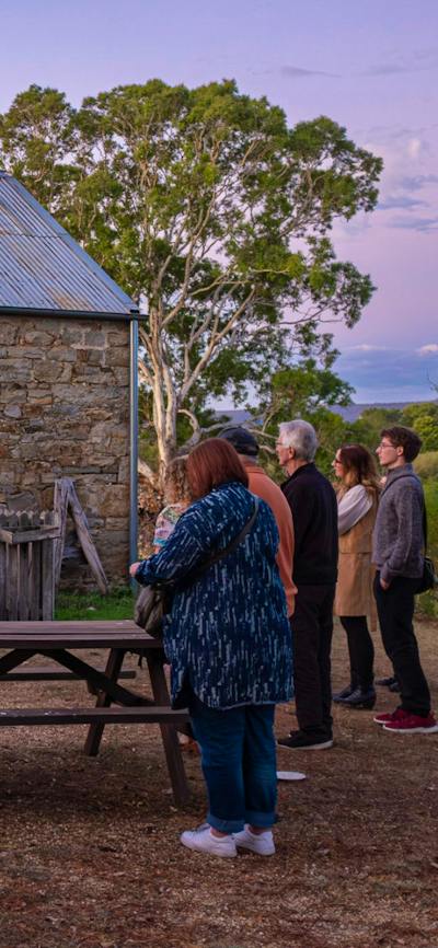 People gather out the front of a stone stable. The light spills out from the doorway as the sun sets