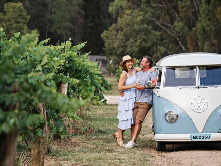 Couple holding wine glasses, next to blue/white VW Kombi
